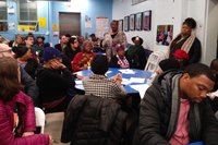 Woman stands and speaks amidst a large group of people assembled around tables