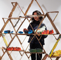 A rendering shows a triangular shelving system constructed with empty produce boxes holding various fruits and vegetables