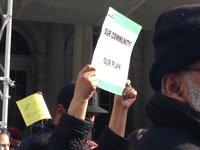 A sign held up at an outdoor protest reads "our community! our plan!"
